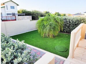 A well-maintained garden with artificial grass, a variety of shrubs, and a small palm tree.