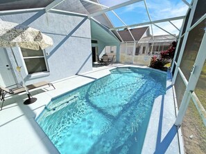 A swimming pool with a glass enclosure, a covered patio area, and a view of a house in the background.