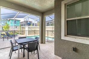 A covered outdoor area with a pool, lounge chairs, and a table.