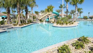 A swimming pool with a water slide, surrounded by palm trees and a clear blue sky.