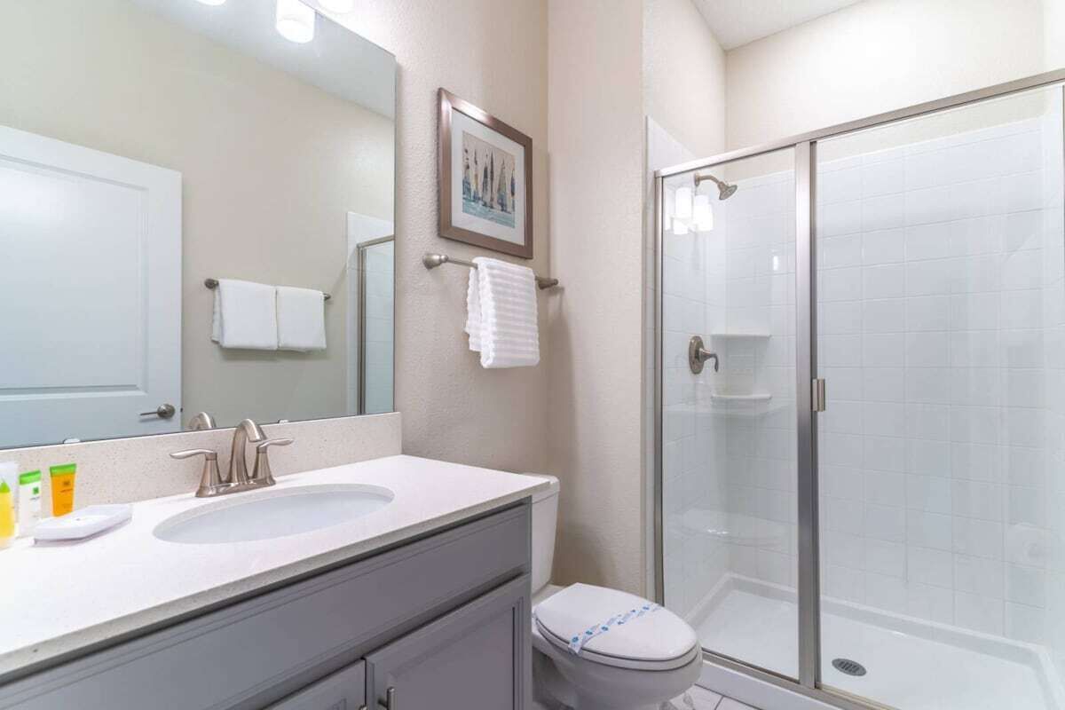 Un baño con un espejo grande, dos lavamanos, un inodoro y una cabina de ducha con paredes de vidrio.