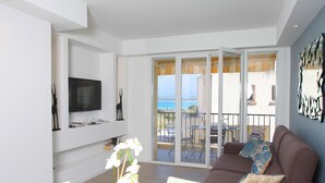A modern living room with a flat-screen TV, a sofa with patterned cushions, a dining table, and a view of the sea through large sliding doors. - Centru : Appart lumineux vue mer, 5 min à pied de la plage et du centre (Calvi)