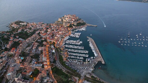 An aerial view of a coastal town with a historic fort, a marina with numerous boats, and a densely built urban area with roads and buildings. - Centru : Appart lumineux vue mer, 5 min à pied de la plage et du centre (Calvi)