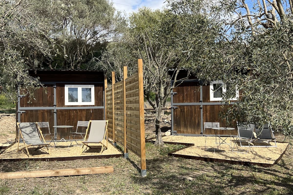 Two wooden cabins with attached patios, each with a table and chairs.