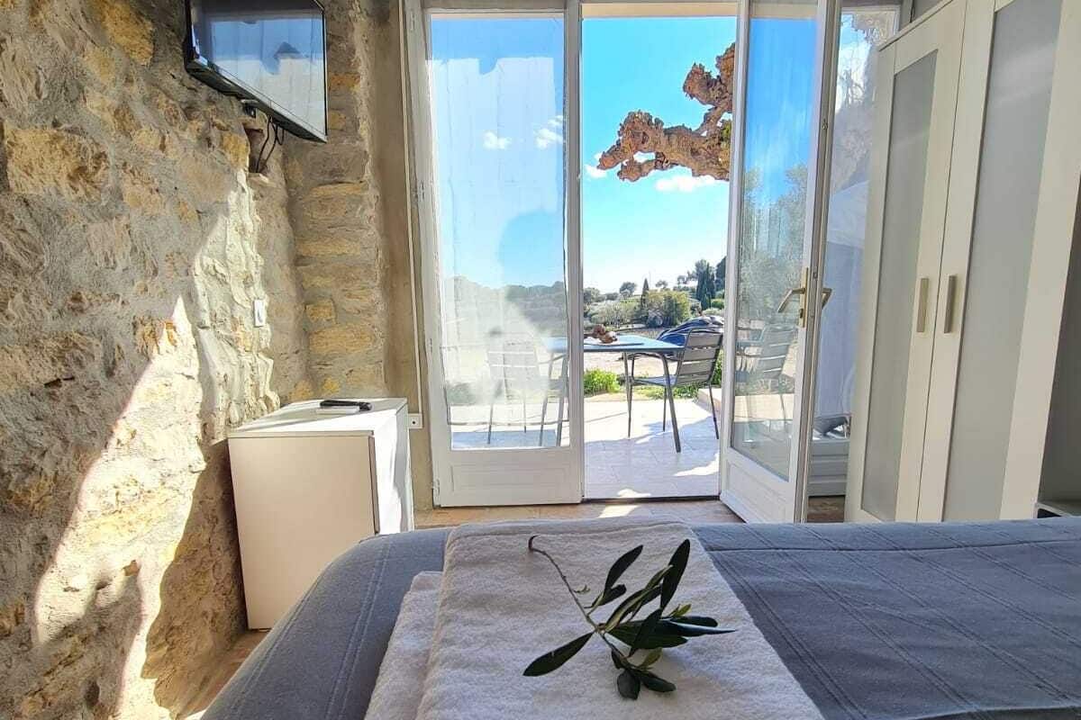 A bedroom with a stone wall, a bed with a folded towel and a branch, a TV mounted on the wall, and a sliding glass door leading to an outdoor area.