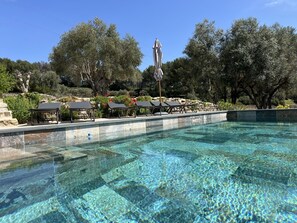 A clear pool with lounge chairs and umbrellas, surrounded by trees and a stone wall. - Le Mas Golie (Le Castellet)