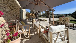 An outdoor patio area with wooden furniture, a large umbrella, and a stone wall. - Le Mas Golie (Le Castellet)