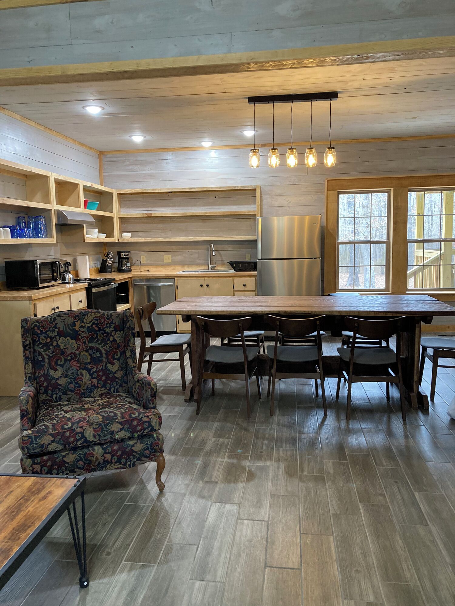 Une cuisine moderne avec des meubles en bois, un réfrigérateur en acier inoxydable et un coin repas comprenant une grande table et des chaises.