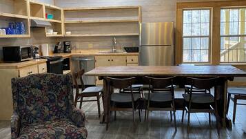 Une cuisine moderne avec des meubles en bois, un réfrigérateur en acier inoxydable et un coin repas comprenant une grande table et des chaises.