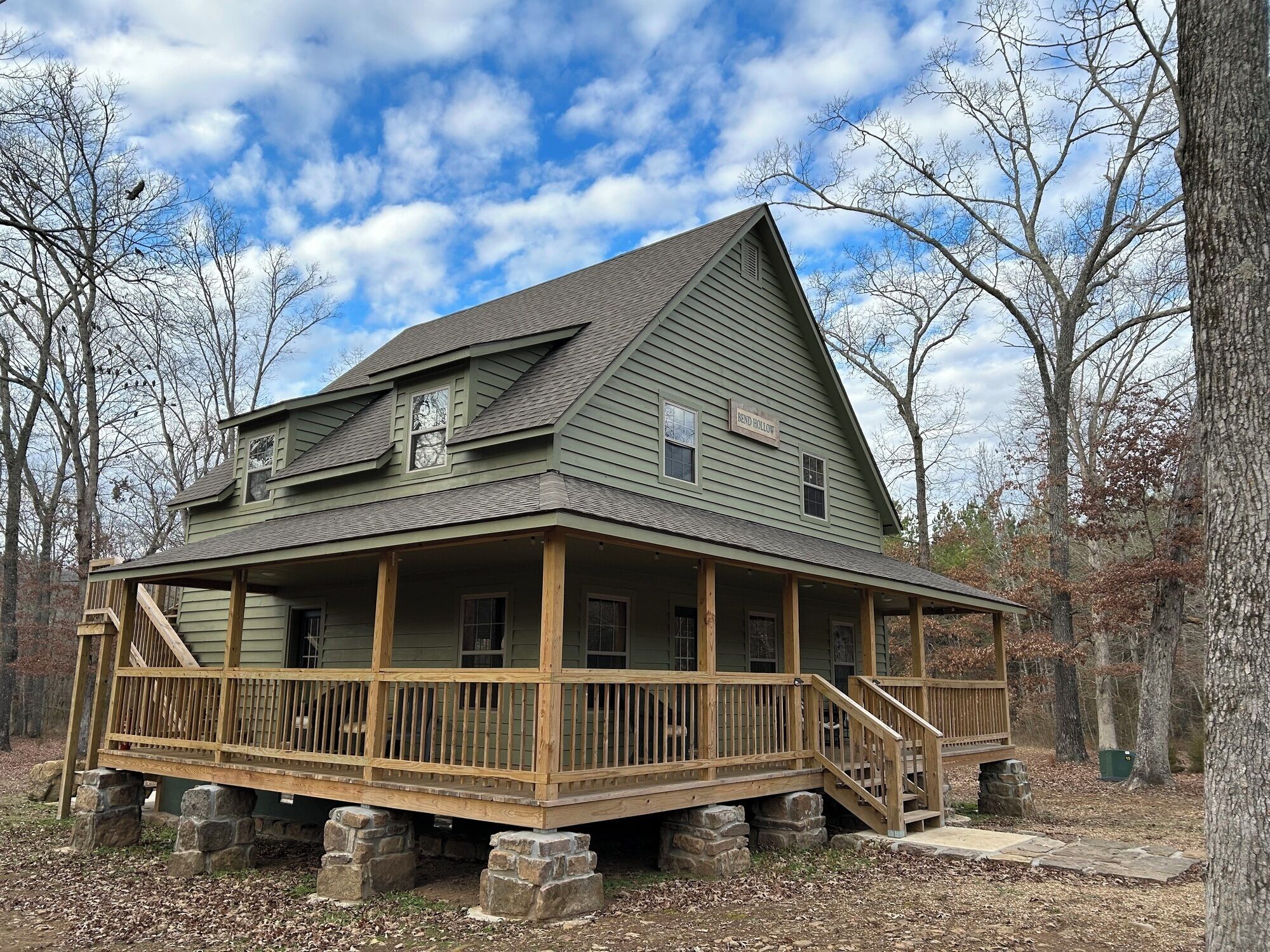 A two-story wooden house with a porch, stone foundation, and a sign that reads 'BEND HOLLOW'.