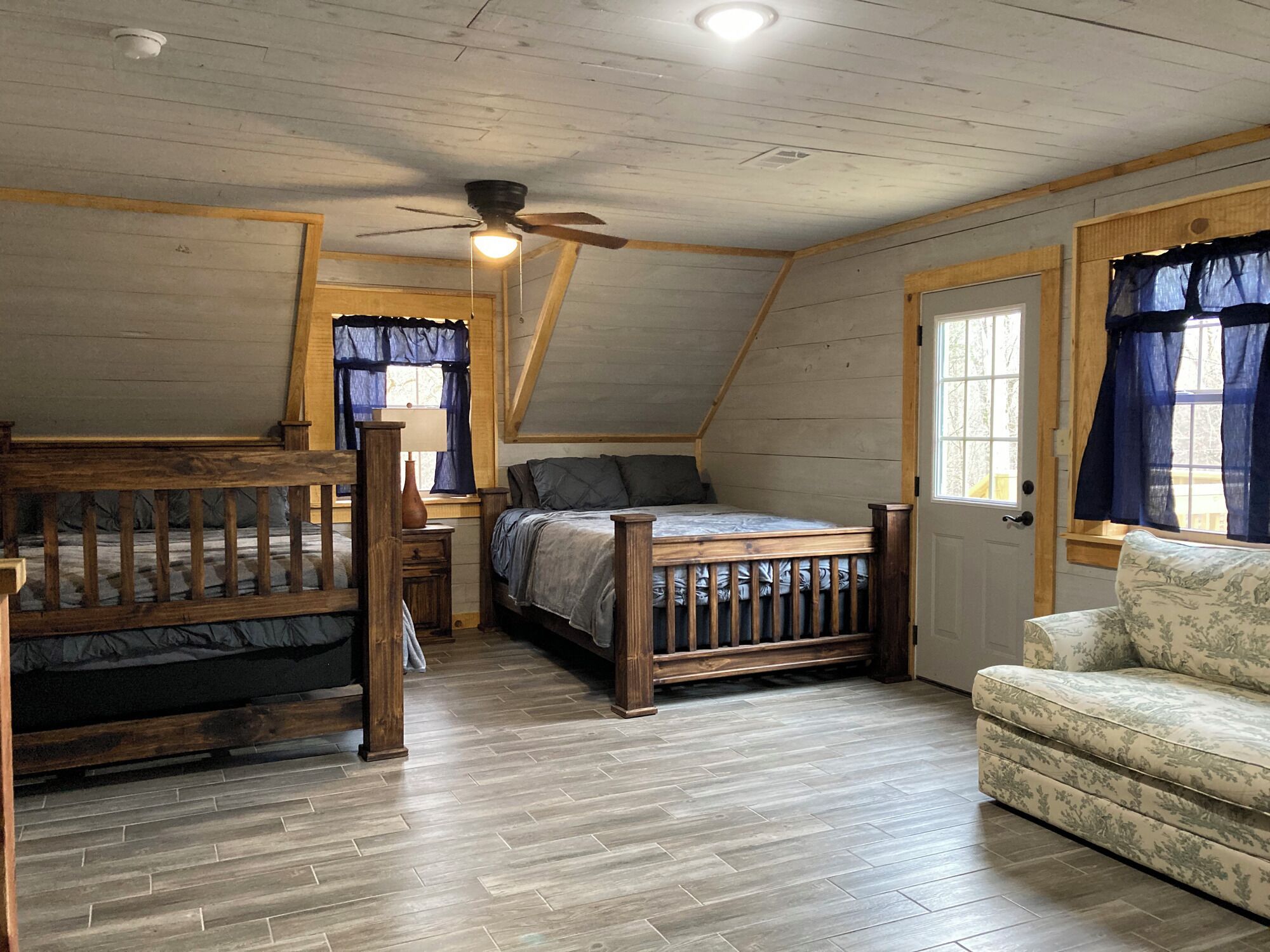 Un dormitorio tipo loft con techo de madera, una cama, una silla y un ventanal con cortinas.
