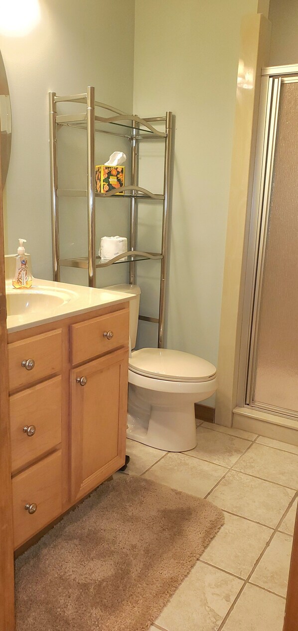 Un baño con tocador de madera, estante de vidrio y zona de ducha, además de un inodoro.