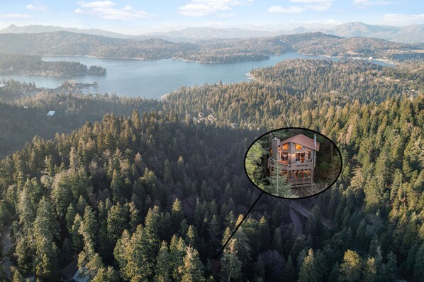 Vista aérea de una zona boscosa con un lago, una casa con terraza y una cadena montañosa al fondo.