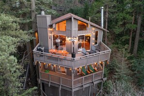 Una cabaña de madera de varios niveles con terraza, mobiliario exterior y chimenea.