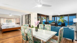 A room with a bed, a dining table with chairs, a sofa, and a view of the ocean.