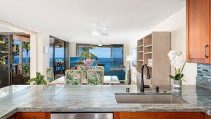 A kitchen with a view of the ocean, a dining area with floral chairs, and a modern design.