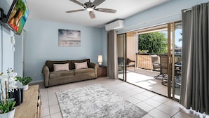 Ein Wohnzimmer mit einer Couch, einem Couchtisch, einem Fernseher, einem Deckenventilator und einer Glastür, die zu einem Außenbereich führt.