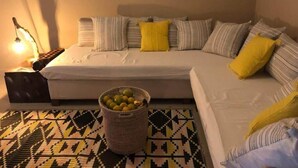 A bedroom with a bed, pillows, a nightstand, a lamp, and a woven basket on a patterned rug. - Villa Citronsverts (Cap skirring)