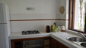 A kitchen with white tiles, a gas stove, a sink, and wooden cabinets. - Villa Citronsverts (Cap skirring)