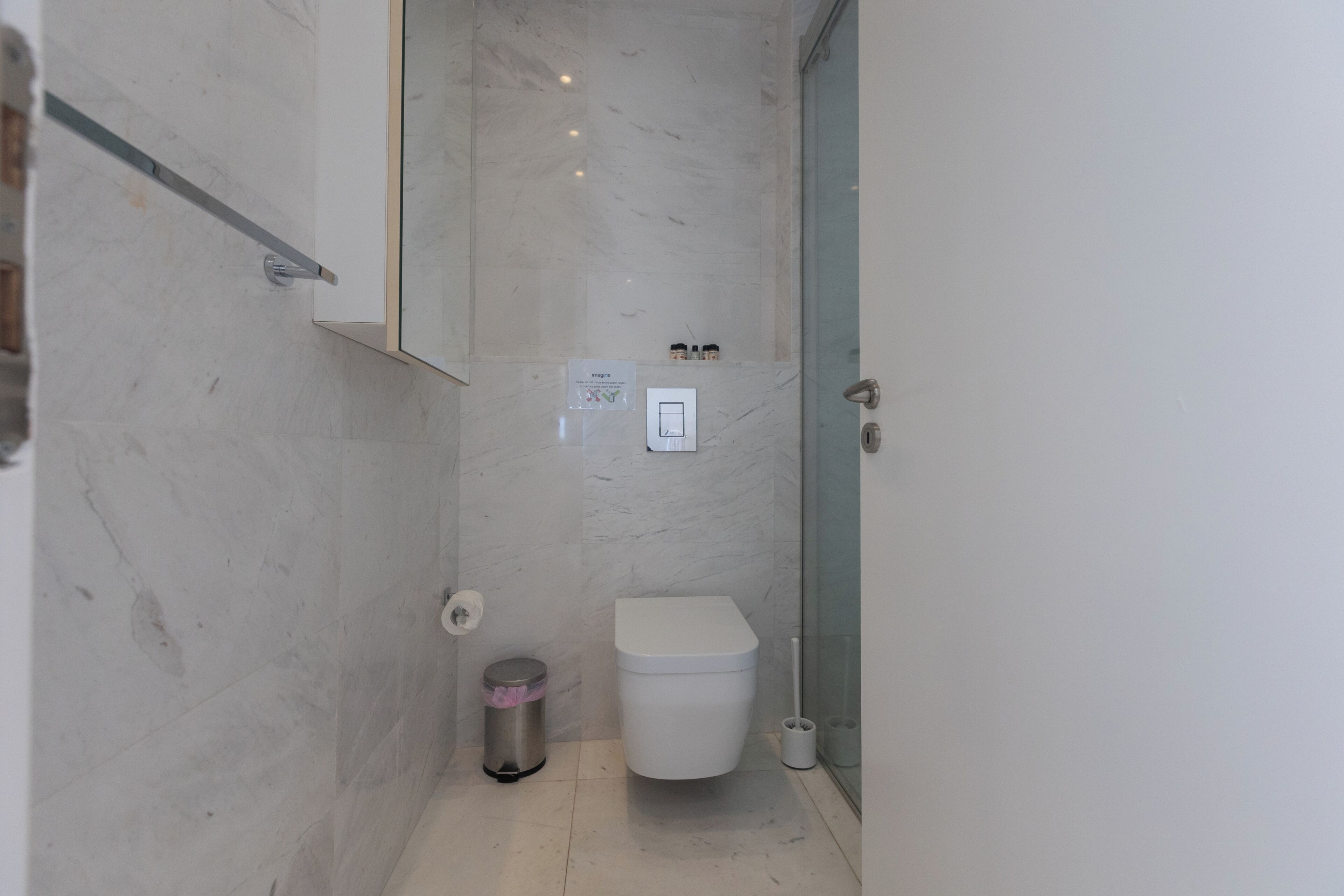 A modern bathroom with a white toilet, a glass shower enclosure, and a marble wall.
