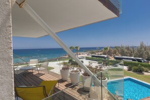 Un balcón con vista al mar, una piscina y mobiliario de exterior.