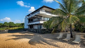 A two-story building with a balcony, a stone wall, and a palm tree.