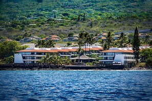 Un hotel costero con varias construcciones, un litoral rocoso y exuberante vegetación al fondo.