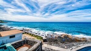 A coastal view with a stone wall, a small building, and a clear blue sky.