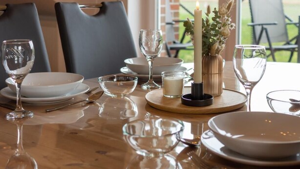 Una mesa de comedor dispuesta con platos blancos, copas de cristal y un centro de mesa con velas.