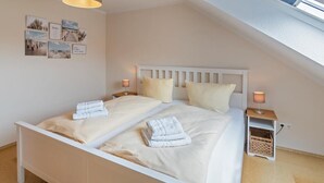 Una cama bien hecha con dos almohadas y toallas dobladas, una mesita de noche con lámpara y una cesta pequeña en el suelo.