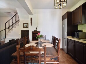 A dining area with a wooden table, chairs, a vase with flowers, a staircase, and a kitchen with a microwave.