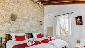 A double room with stone walls, two beds with red and white bedding, a wooden floor, and a window with curtains. - Sanders Arsorama Comfy 1 Bdr Apt w Shared Patio (Arsos)
