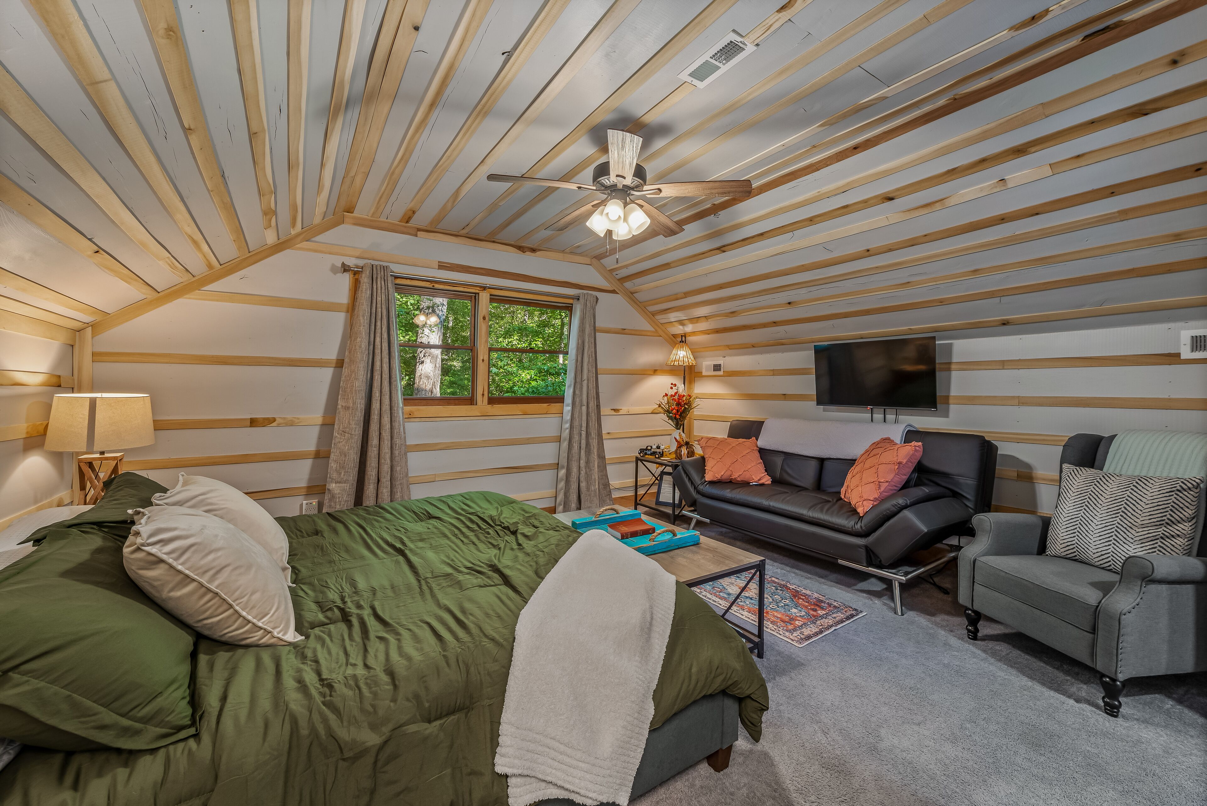 A cozy room with a bed, a sofa, a chair, a TV, and a ceiling fan.