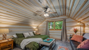 A cozy bedroom with a bed, bedside table, lamp, and a view of greenery outside.