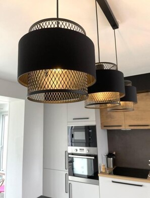 A modern kitchen with stainless steel appliances, wooden cabinets, and a black pendant light fixture. - Nouveauté Plouescat, Grande Maison vue mer Pour 8 Personnes (Plouescat)