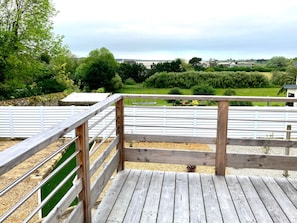 A wooden deck with a metal railing overlooking a green landscape with trees and a distant view of buildings. - Nouveauté Plouescat, Grande Maison vue mer Pour 8 Personnes (Plouescat)