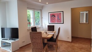 A dining area with a TV, wicker chairs, a table, and a painting on the wall.