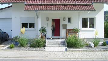 Ein zweistöckiges Haus mit rotem Ziegeldach, einer Haustür und einer kleinen Veranda mit Stufen zum Eingang.