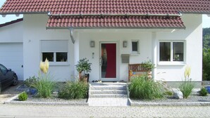 A two-story house with a red-tiled roof, a red front door, and a small porch with steps.