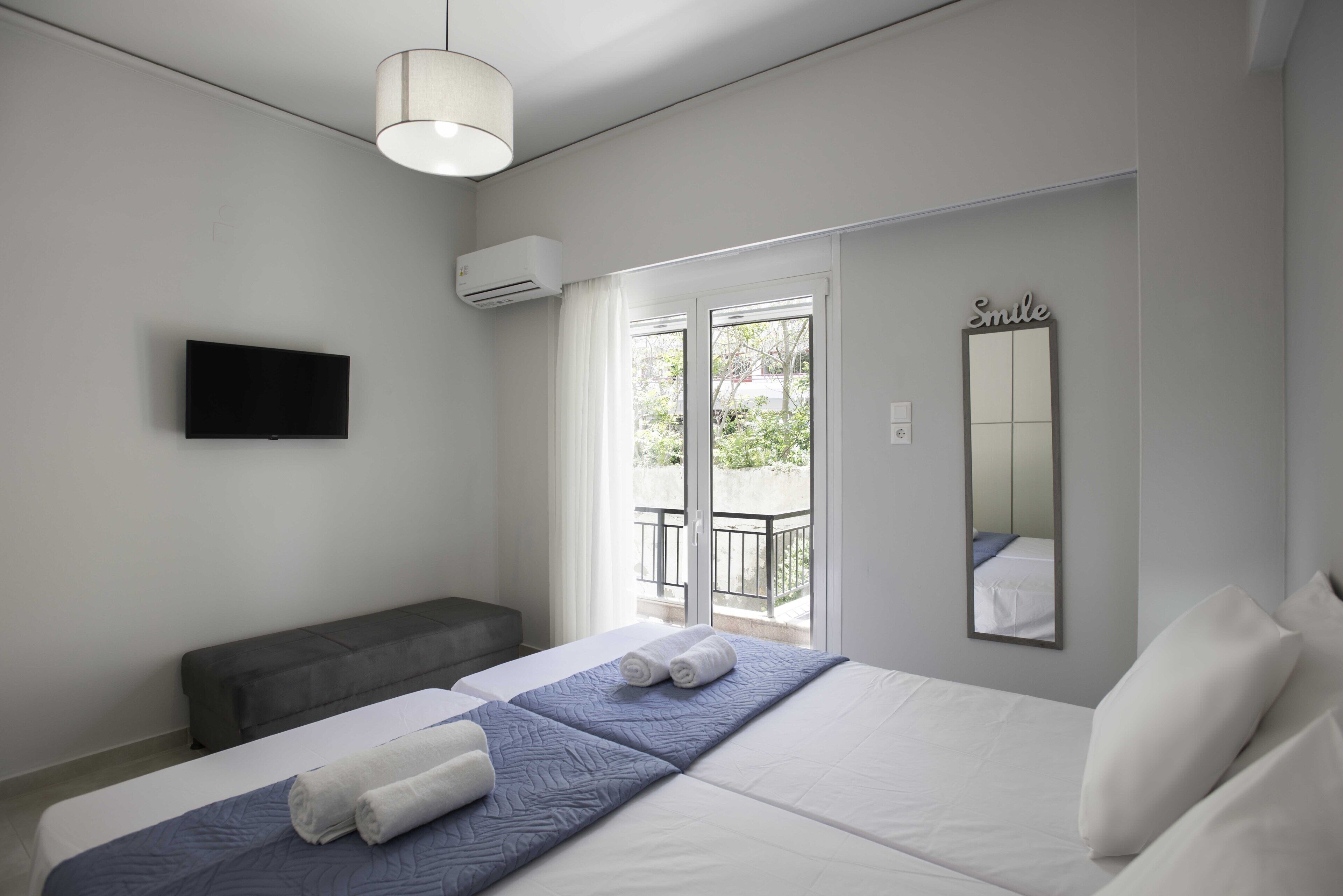 Ein modernes Hotelzimmer mit einem großen Bett, einer Sitzbank, einem Flachbildfernseher, einer Klimaanlage und einem Balkon mit Blick.
