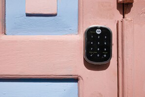 A keypad door lock mounted on a wall with a blue and pink color scheme. - Hostted (Flores)