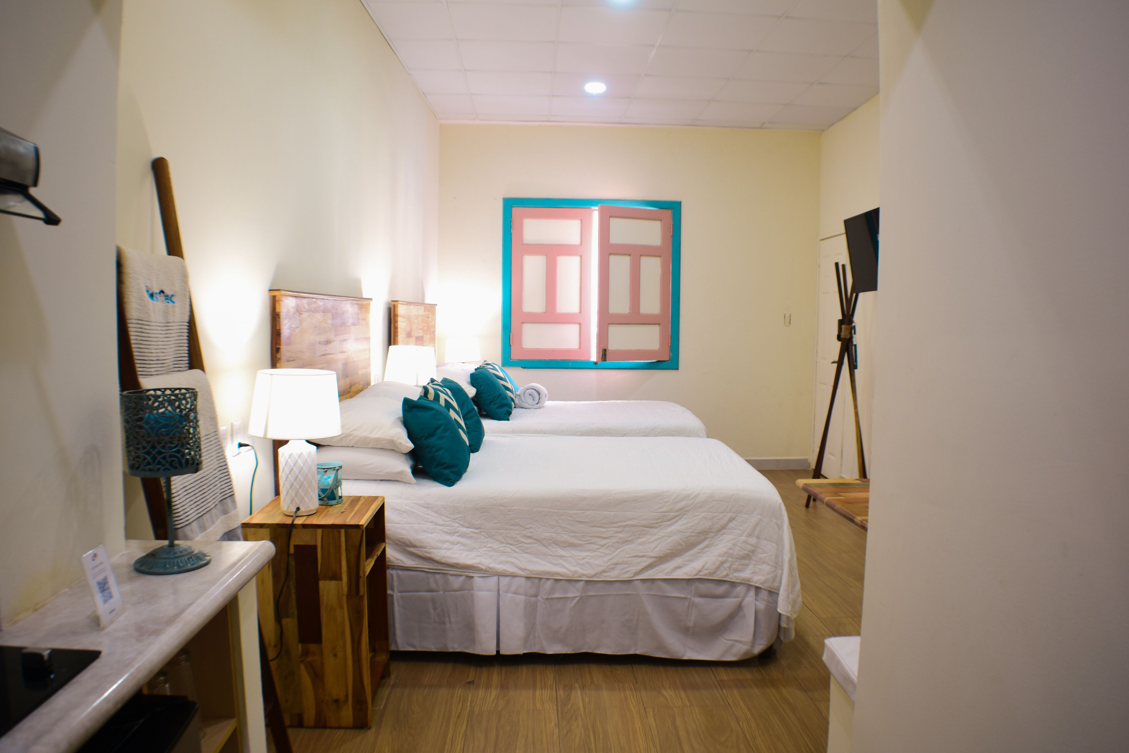Una camera d'albergo con due letti, una scrivania, una lampada e un'ampia finestra con cornice blu.