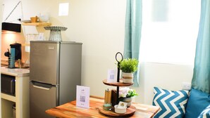 A compact kitchen with a refrigerator, a wooden table with a tray, and a small seating area with a sofa and pillows. - Hostted (Flores)