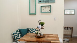 A cozy corner with a wooden table, a bench with teal cushions, and a wall-mounted air conditioner. - Hostted (Flores)