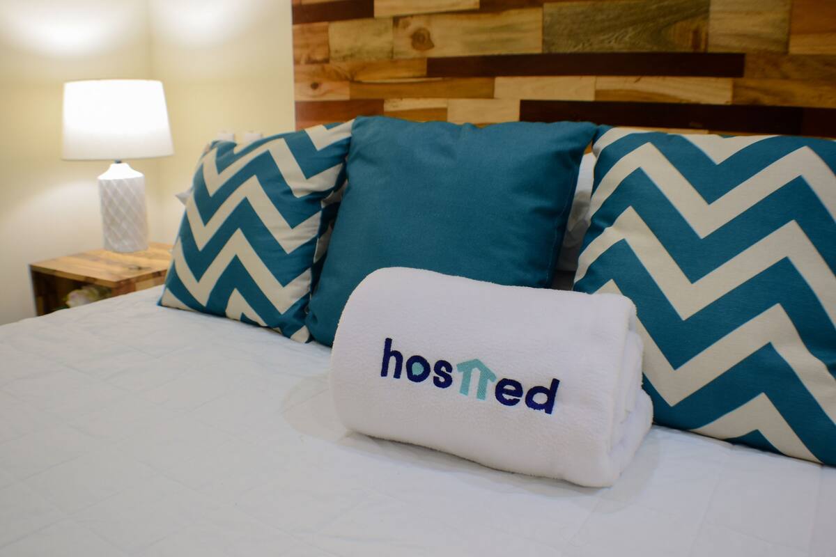 A neatly made bed with a pillow that reads "hosted" and a decorative headboard.