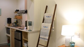 A compact kitchen with a wooden ladder leaning against the wall, a small table with a lamp, and a refrigerator. - Hostted (Flores)