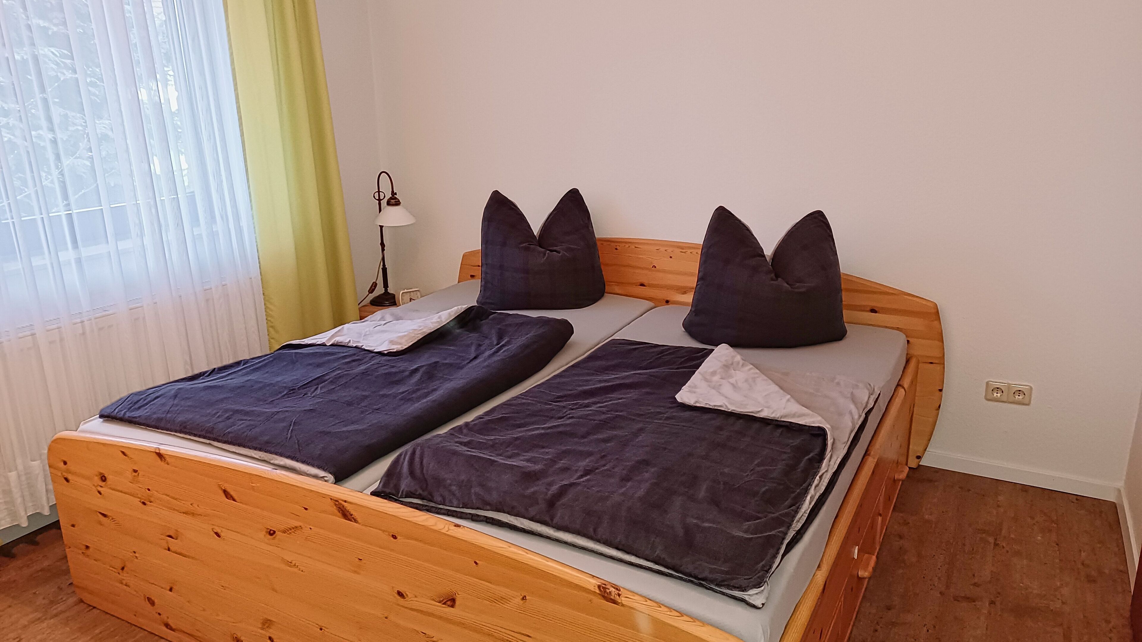 Ein Doppelbett mit Holzrahmen, zwei Kissen und einer Nachttischlampe.
