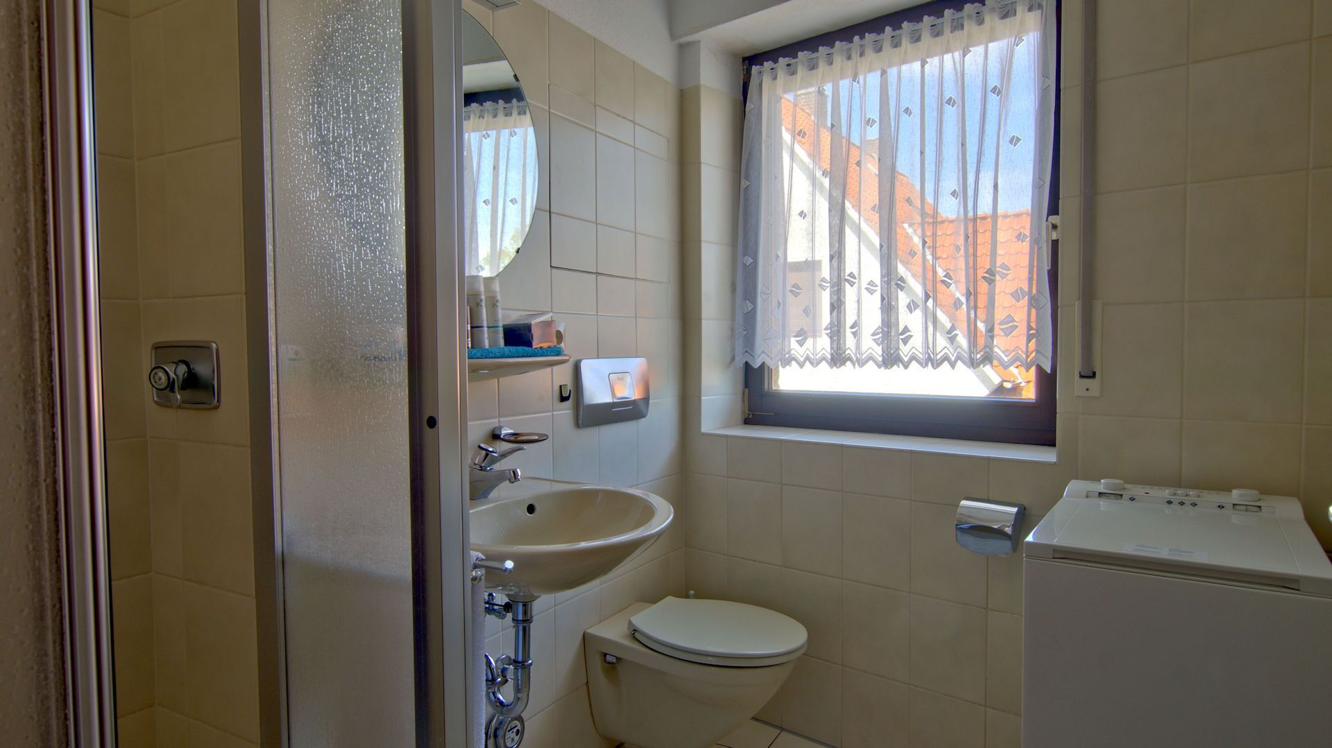 Ein kleines Badezimmer mit Toilette, Waschbecken und einem Fenster mit Vorhängen.