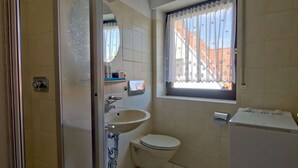 A compact bathroom with a toilet, sink, and a small window with curtains.