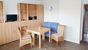 A room with a wooden cabinet, a blue sofa, a wicker chair, a table, and a television.